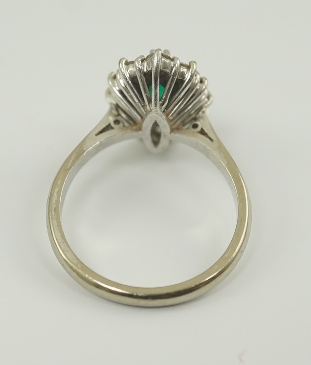 A modern 18ct white gold and single stone marquise cut emerald set ring, bordered with round brilliant cut diamonds